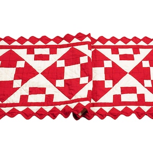 May include: Red and white quilted table runner with a scalloped edge. The runner features a geometric pattern of squares and diamonds.