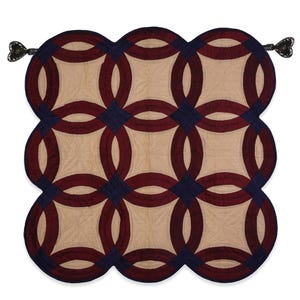 May include: A burgundy and navy blue quilted wall hanging with a double ring pattern. The wall hanging has a scalloped edge and two tassels.