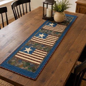 May include: A rectangular table runner with a patriotic design featuring stars and stripes. The runner has a blue border and is placed on a wooden table. A candle lantern and a vase with greenery are on the table.