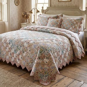 May include: A floral quilt set on a bed, featuring a patchwork design with a scalloped edge. The set includes a quilt and matching pillowcases. The color palette includes shades of pink, blue, and cream, creating a vintage aesthetic.