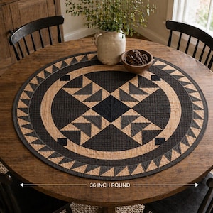 Peut inclure: Un napperon de table rond noir et beige avec un motif géométrique, mesurant 91 cm de diamètre. Le napperon présente un motif central en forme d'étoile et une bordure de triangles. Il est posé sur une table en bois avec des chaises noires.