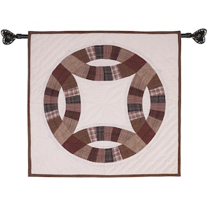 May include: A brown and cream quilted wall hanging with a circular design featuring a ring pattern. The design is made up of various shades of brown and cream plaid fabric.