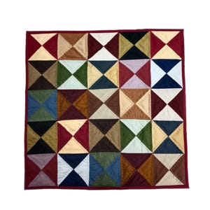 May include: A square quilt with a patchwork design. The quilt features a repeating pattern of squares, each divided into four triangles of various colors, including red, brown, beige, green, and blue. The quilt is bordered with a solid maroon fabric.