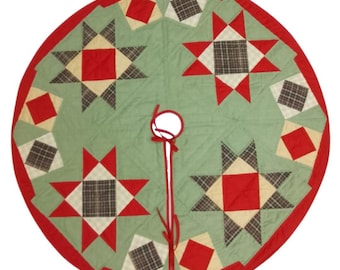 May include: A round Christmas tree skirt with a green center, red border, and star and diamond patchwork design. The patchwork includes red, cream, and plaid squares. A white circle and red ribbon are at the center.