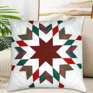 Puede incluir: Cojín cuadrado blanco con un patrón acolchado y un diseño central de estrella. La estrella está compuesta por piezas de tela rojas, verdes y a cuadros. Para la decoración del hogar.