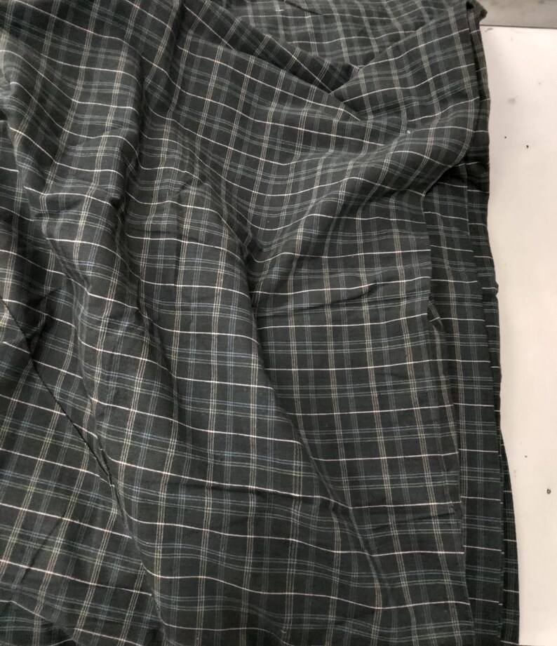 May include: Dark green plaid fabric with white and light blue lines. The fabric is folded and draped, creating shadows and texture. The pattern is a classic grid design, suitable for apparel or home decor.