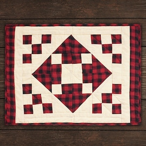 Può includere: Un runner da tavolo a quadri rosso e bianco con un motivo a rombi al centro. Il runner è realizzato in tessuto e ha una texture trapuntata.