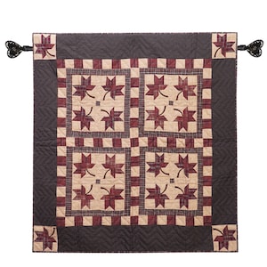 Könnte beinhalten: Ein quadratischer Wandbehang mit einem sich wiederholenden Muster aus dunkelroten, karierten Ahornblättern auf cremefarbenem Grund. Der Quilt ist mit einem dunkelbraunen Rand mit Zickzack-Steppmuster und einem karierten Innenrand eingefasst.
