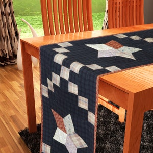 May include: A blue and white quilted table runner with a star design. The runner is on a wooden table with two chairs.