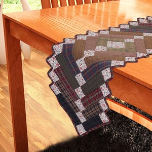 May include: A patchwork table runner with a scalloped edge. The runner is made of various plaid and floral fabrics in shades of green, brown, red, and blue.