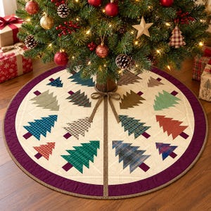 May include: A circular quilted Christmas tree skirt featuring a cream-colored base with a wide purple border. The surface is decorated with various fabric Christmas tree appliques in assorted plaid, checkered, and solid patterns. A brown ribbon tie is at the center.