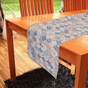 May include: A beige and blue patchwork table runner with a diamond pattern. The runner is on a wooden table with two chairs.