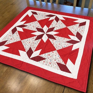May include: Red, white, and burgundy quilt with a geometric star pattern. The quilt has a white border and a red outer border.