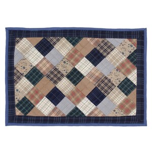 Puede incluir: Un mantel individual acolchado de patchwork azul y marrón con un patrón de diamantes. El mantel individual tiene un borde azul.