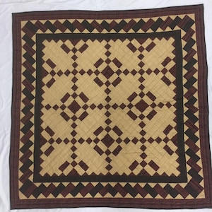 May include: A brown and tan quilt with a geometric pattern. The quilt has a dark brown border with a diamond pattern.