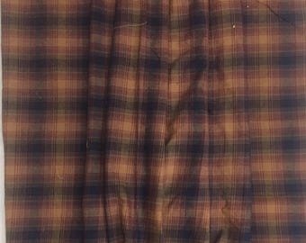May include: A close-up of a brown and tan plaid fabric with a subtle green hue. The fabric is folded in half and has a soft, textured appearance.