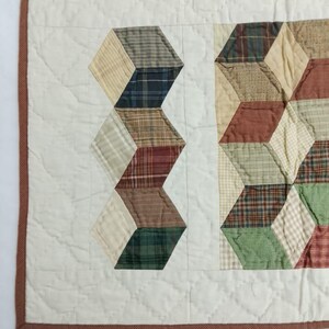 May include: A handmade quilt with a geometric design. The quilt features alternating columns of white fabric and colorful, plaid-patterned blocks in shades of green, brown, and red. The quilt is bordered with a brown fabric.