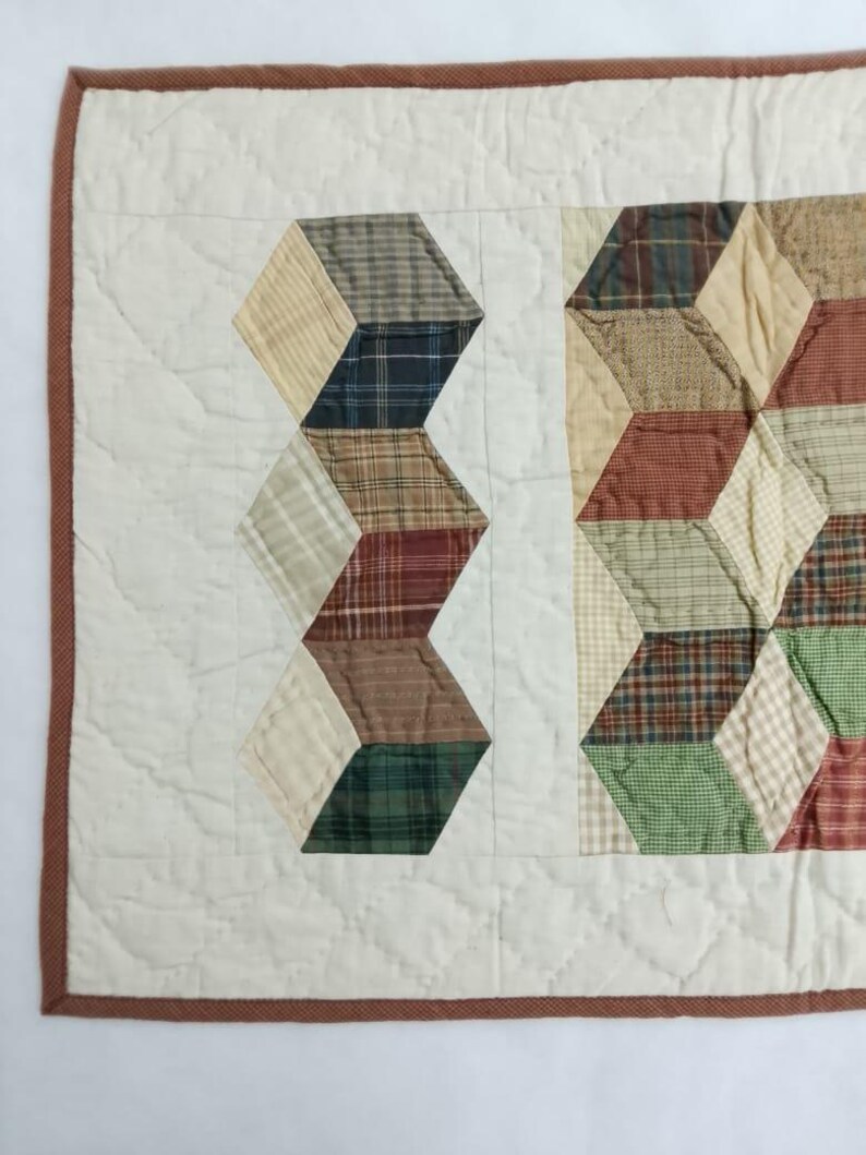 May include: A handmade quilt with a geometric design. The quilt features alternating columns of white fabric and colorful, plaid-patterned blocks in shades of green, brown, and red. The quilt is bordered with a brown fabric.