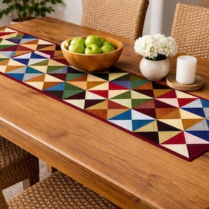 Könnte beinhalten: Ein Holztisch ist mit einem farbenfrohen, geometrisch gemusterten Tischläufer gedeckt. Eine Holzschale enthält grüne Äpfel, und eine weiße Vase mit weißen Blumen und eine Kerze vervollständigen die Dekoration.