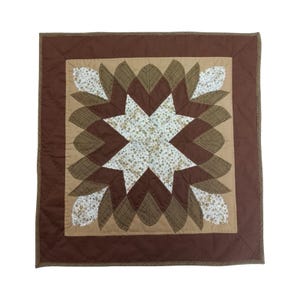 May include: A square, handmade quilt with a starburst design. The quilt features a central star in white floral fabric, surrounded by brown and tan petal-shaped elements. The border is a solid dark brown.
