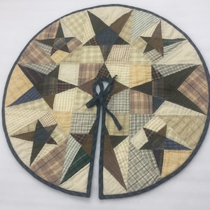 May include: A patchwork quilt tree skirt with a blue denim trim and a tie closure. The skirt is made of various shades of brown, beige, and green plaid fabric and features a star design.