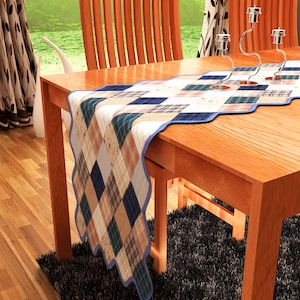 May include: A patchwork table runner with a blue border and scalloped edges. The runner is laid on a wooden table with two chairs.
