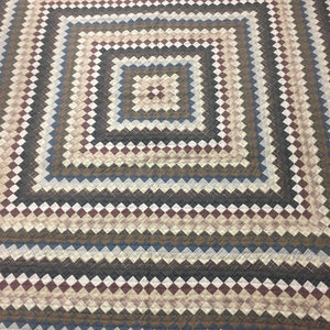 Könnte beinhalten: Eine braune, beige und blaue Steppdecke mit einem quadratischen Muster. Die Steppdecke hat einen gewellten Rand.