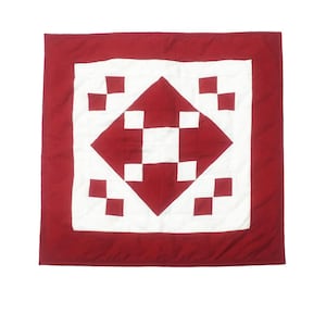 May include: A red and white quilt with a geometric pattern. The quilt is made of squares and diamonds. The center of the quilt is a large white diamond with a red cross in the center.