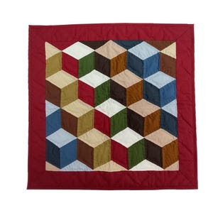 May include: A handmade quilt featuring a geometric cube design in shades of red, blue, green, and brown. The quilt has a solid red border. The design creates a 3D effect. The quilt is likely made of cotton fabric.
