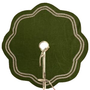 Op de afbeelding: Een groene kerstboomrok met een geschulpte rand en zilveren afwerking. De rok heeft een centrale opening voor de boomstam en wordt ondersteund door een zilveren standaard.