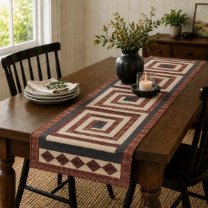 Può includere: Un runner da tavola rettangolare con un motivo geometrico di quadrati concentrici e rombi nei toni del ruggine, crema e blu navy scuro. Il runner è steso su un tavolo in legno, accompagnato da tovaglioli bianchi e un vaso nero.
