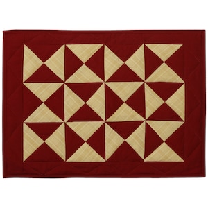 May include: A red and cream quilted placemat with a geometric pattern of alternating triangles. The placemat has a stitched border.