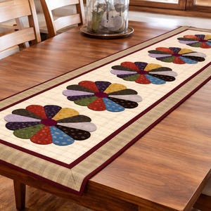 Puede incluir: Camino de mesa rectangular con un centro crema con un patrón floral repetido en varios colores. El camino de mesa tiene un borde burdeos y está colocado sobre una mesa de madera. El diseño floral incluye pétalos rojos, azules, amarillos y morados. Mide unos 150 cm.