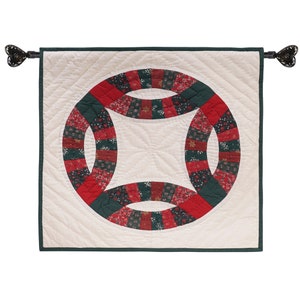 May include: A white quilted wall hanging with a green and red double ring design. The rings are made of fabric with a floral pattern.