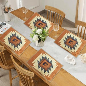 May include: A wooden dining table set with four square placemats and a long table runner. The placemats and runner feature a geometric design in shades of orange, cream, and blue. The table is set with flowers, glasses, and a coffee cup.
