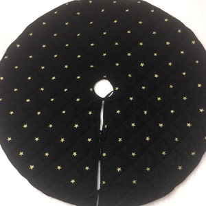 May include: Black quilted Christmas tree skirt with gold stars. The skirt has a tie closure.
