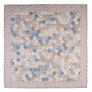 May include: A white quilt with a hexagonal pattern. The quilt is made of various floral fabrics in shades of blue, pink, and beige. The quilt has a red and white floral border.