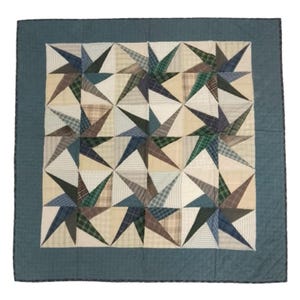 May include: A square quilt with a starburst pattern. The quilt has a teal border and a central design of alternating star shapes in various plaid and solid fabrics, including beige, green, and blue. The quilt is likely handmade.
