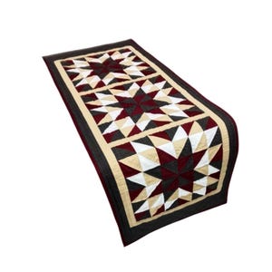 Könnte beinhalten: Ein rechteckiger, gesteppter Tischläufer mit Sternmuster. Der Läufer hat ein dunkelrotes, cremefarbenes und weißes Sterndesign, das von einem cremefarbenen und schwarzen Stoff umrandet ist. Die Kanten sind mit einem dunkelroten und schwarzen Stoff versehen.