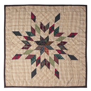 May include: A square quilt with a central starburst design. The star is composed of diamond-shaped patches in various plaid patterns, including red, green, and black. The background is a beige plaid fabric, and the quilt has a dark brown border.