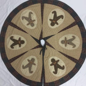 Puede incluir: Una falda de árbol de Navidad acolchada marrón y beige con un borde de cuadros. Seis hombres de jengibre están aplicados en la falda.