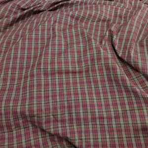 May include: Close-up of a fabric with a plaid pattern. The fabric features a burgundy base with intersecting lines in black and light green, creating a classic plaid design. The fabric is slightly wrinkled.