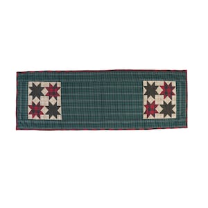 May include: A green and red plaid table runner with two red and black star blocks. The runner has a green and white plaid background.