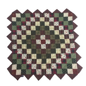 Peut inclure: Une courtepointe patchwork rouge, verte et crème avec un bord festonné. La courtepointe est faite de carrés de tissus différents, y compris du plaid, des fleurs et des couleurs unies.
