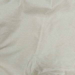 May include: Close-up of a light beige fabric with a small, evenly spaced checkered pattern. The fabric is slightly wrinkled, creating shadows and variations in tone. The overall appearance suggests a soft, woven material, possibly cotton or linen.