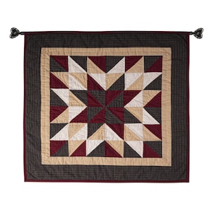May include: A burgundy, black, and cream quilted wall hanging with a starburst pattern. The hanging has a black and white checkered border and tassels on each corner.