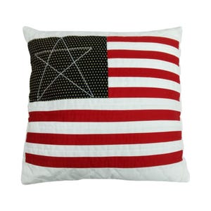 May include: A white pillow with a red, white, and blue American flag design. The flag is quilted and has a black star in the upper left corner.