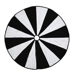 May include: A round, black and white tree skirt with a striped pattern. The skirt is divided into alternating black and white pie-shaped sections radiating from a central opening. The white sections have a textured, quilted appearance.