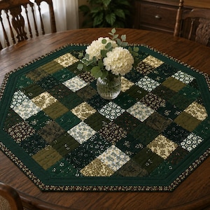 May include: An octagonal quilted table runner with a patchwork design in shades of green, cream, and brown. The runner features a floral pattern and a dark green border. A vase of white flowers sits in the center.