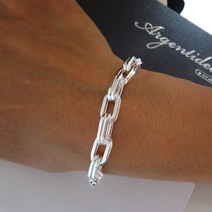 May include: A silver chain link bracelet is shown on a wrist. The bracelet is made of polished metal and features a series of elongated, rectangular links. The bracelet is shown against a dark background with the brand name "Argentidea" visible.